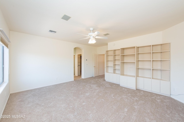 empty room with arched walkways, light carpet, visible vents, and a ceiling fan