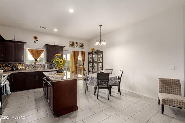 kitchen with light stone countertops, sink, pendant lighting, a chandelier, and a center island