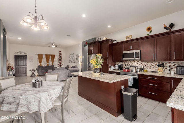 kitchen with light stone countertops, ceiling fan with notable chandelier, decorative light fixtures, and appliances with stainless steel finishes