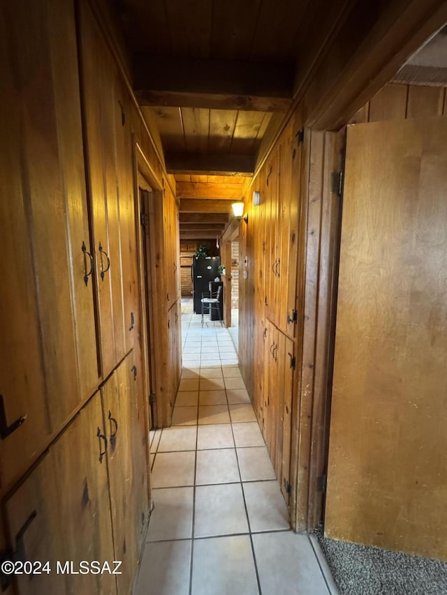 hallway featuring wooden walls, beamed ceiling, light tile patterned floors, and wooden ceiling