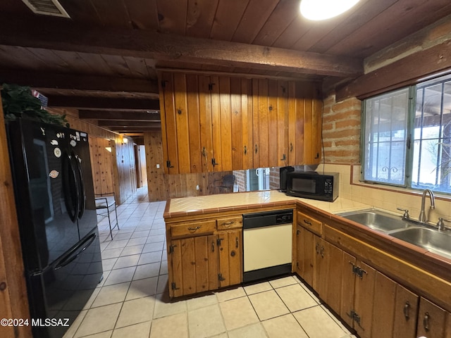 kitchen with beam ceiling, tile counters, wood walls, light tile patterned flooring, and black appliances