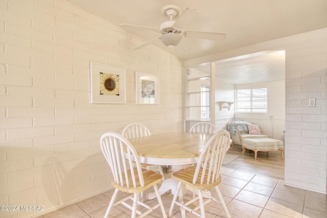 tiled dining room with ceiling fan and brick wall