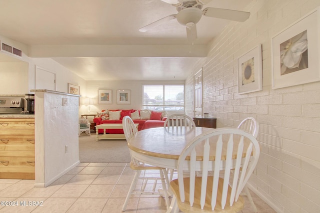 tiled dining space with ceiling fan and brick wall