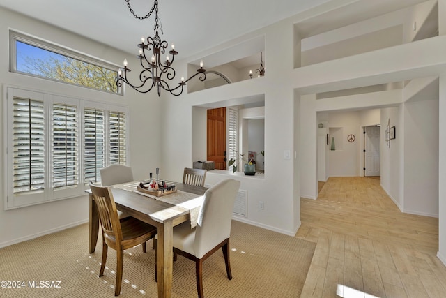 dining area with a high ceiling, light hardwood / wood-style floors, and an inviting chandelier