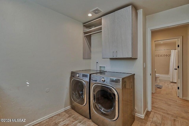 laundry room with washer and clothes dryer, cabinets, and light hardwood / wood-style flooring