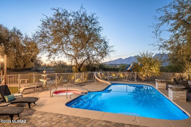 pool at dusk featuring a mountain view, a patio, and a water slide