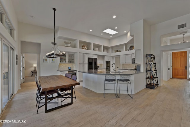 kitchen with a skylight, white cabinetry, tasteful backsplash, a towering ceiling, and black refrigerator