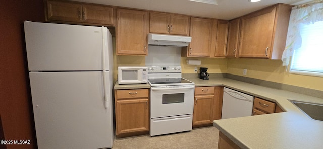 kitchen featuring white appliances, brown cabinets, light countertops, under cabinet range hood, and a sink