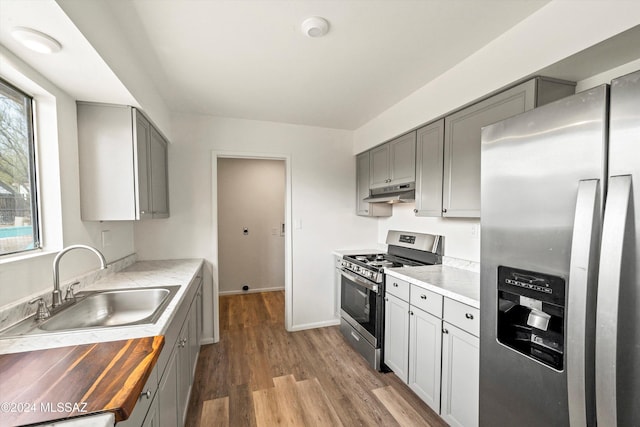 kitchen with gray cabinetry, sink, wooden counters, appliances with stainless steel finishes, and hardwood / wood-style flooring