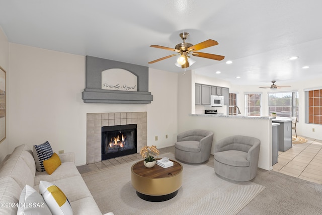 carpeted living room with ceiling fan, sink, and a tile fireplace