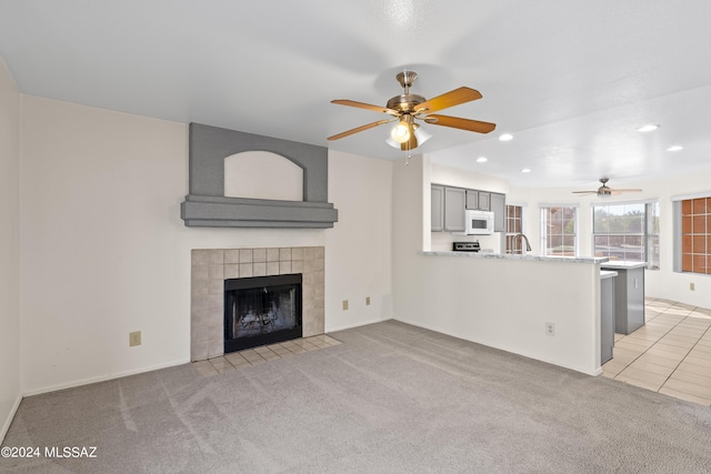 unfurnished living room featuring light carpet, a tile fireplace, and ceiling fan