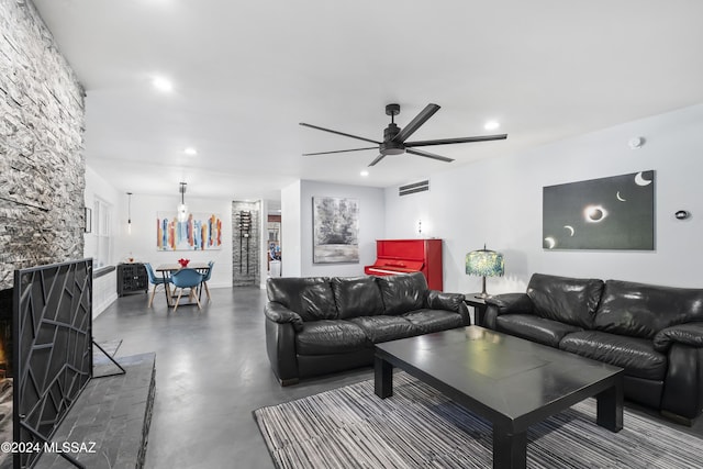 living room featuring concrete floors, a stone fireplace, and ceiling fan