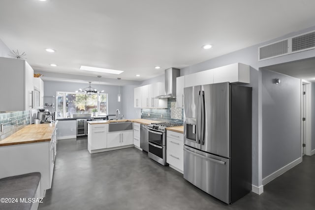 kitchen with a skylight, white cabinetry, wall chimney exhaust hood, butcher block countertops, and appliances with stainless steel finishes