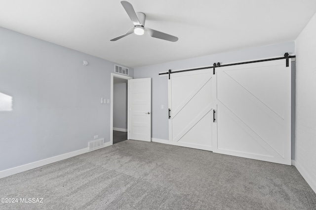 unfurnished bedroom featuring carpet flooring, a barn door, and ceiling fan