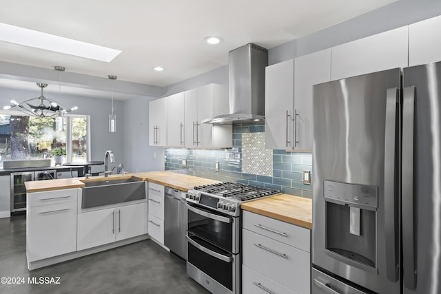 kitchen featuring sink, wall chimney exhaust hood, hanging light fixtures, white cabinets, and appliances with stainless steel finishes