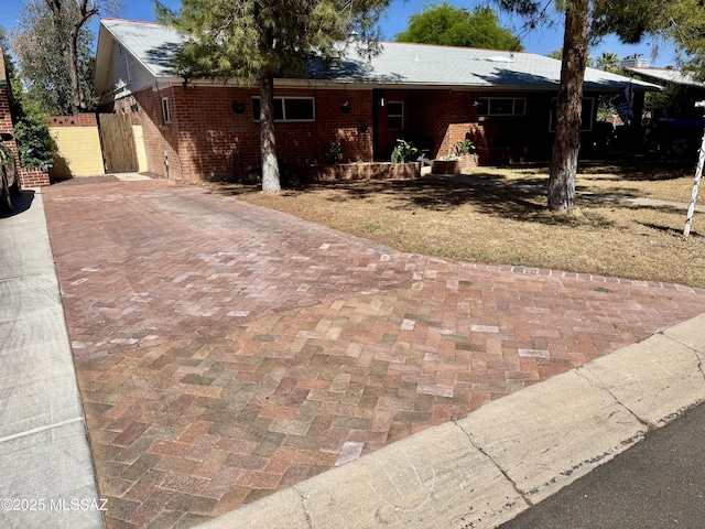 ranch-style house featuring brick siding, fence, and decorative driveway