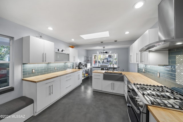 kitchen featuring stainless steel gas stove, wall chimney range hood, wood counters, decorative light fixtures, and white cabinets