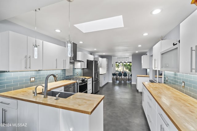 kitchen featuring a skylight, stainless steel appliances, wooden counters, decorative light fixtures, and white cabinets