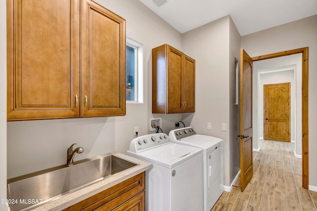 clothes washing area featuring washer and clothes dryer, sink, cabinets, and light hardwood / wood-style floors