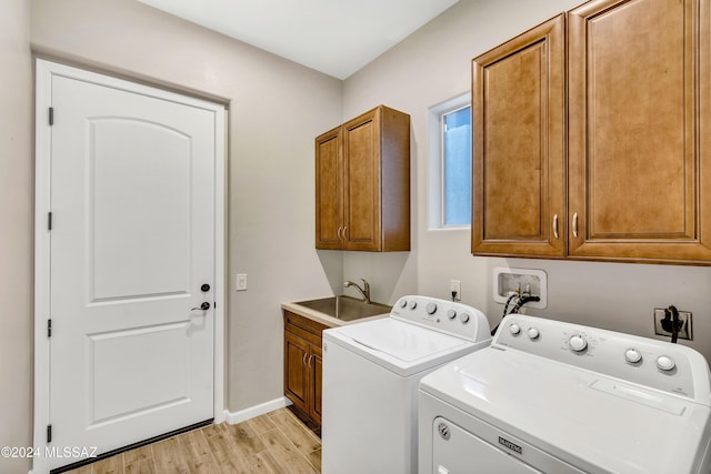 laundry room featuring washing machine and dryer, sink, cabinets, and light hardwood / wood-style flooring