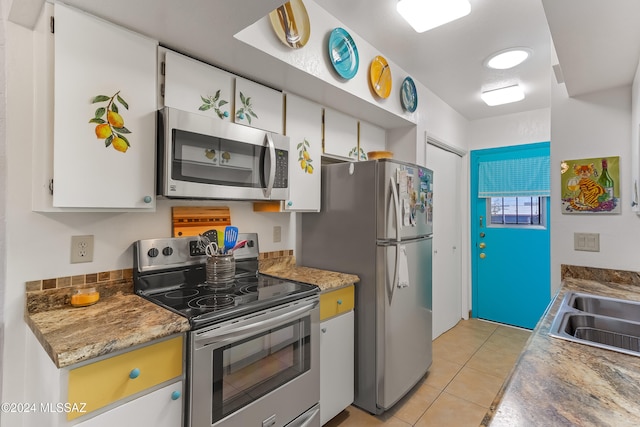 kitchen with white cabinets, appliances with stainless steel finishes, dark stone counters, and light tile patterned flooring