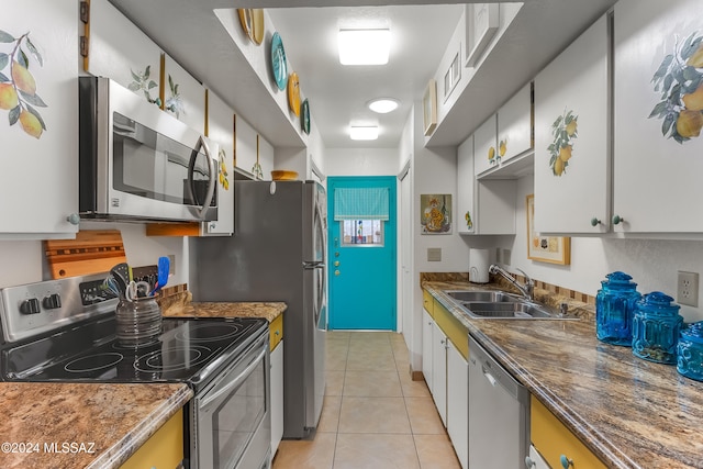 kitchen featuring appliances with stainless steel finishes, sink, dark stone countertops, white cabinets, and light tile patterned flooring