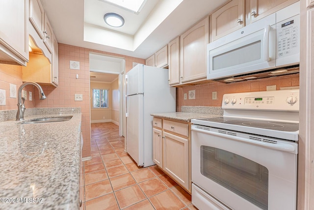 kitchen with light brown cabinets, white appliances, sink, light tile patterned floors, and a tray ceiling