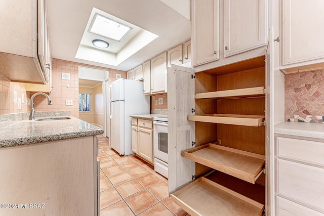 kitchen featuring sink, a skylight, white fridge, light stone counters, and range