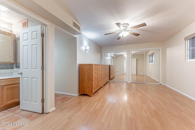 unfurnished bedroom featuring multiple closets, ceiling fan, ensuite bathroom, light hardwood / wood-style floors, and a textured ceiling