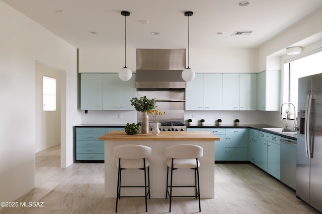 kitchen with pendant lighting, a center island, wall chimney range hood, sink, and stainless steel appliances