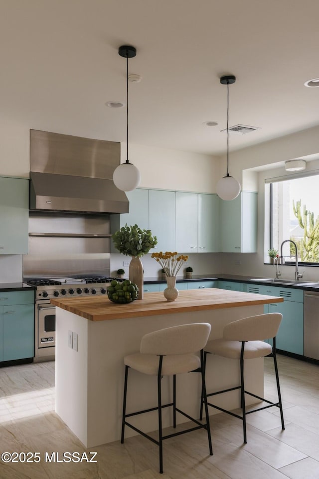 kitchen with wall chimney range hood, premium stove, sink, and decorative light fixtures