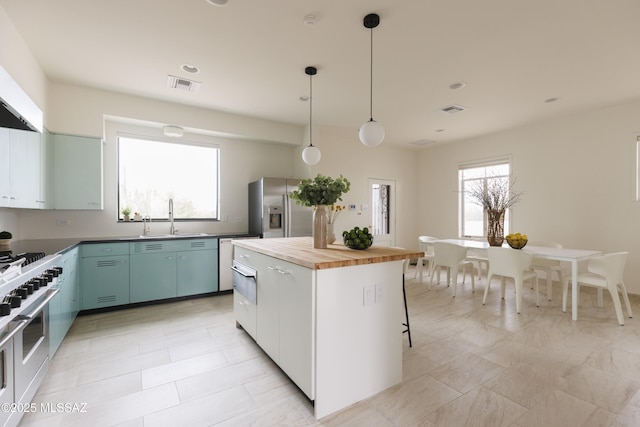 kitchen featuring wooden counters, stainless steel appliances, sink, a kitchen island, and hanging light fixtures