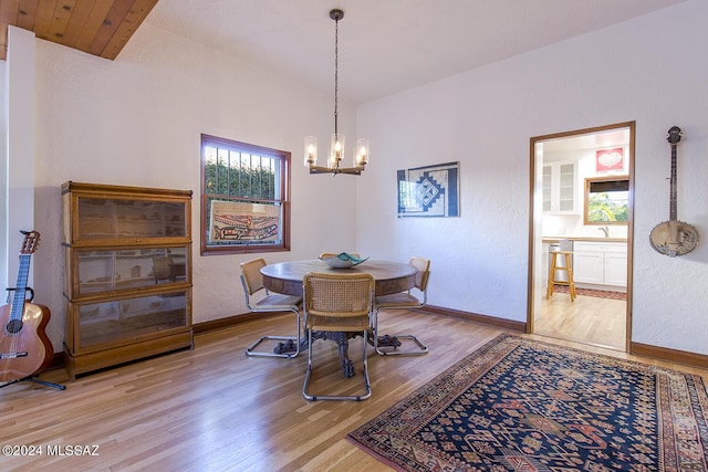 dining space with light wood-type flooring, an inviting chandelier, vaulted ceiling, and sink