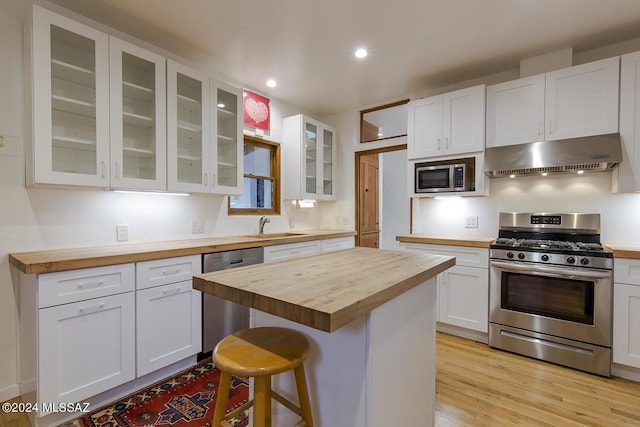 kitchen with stainless steel appliances, a breakfast bar area, a center island, white cabinetry, and butcher block counters