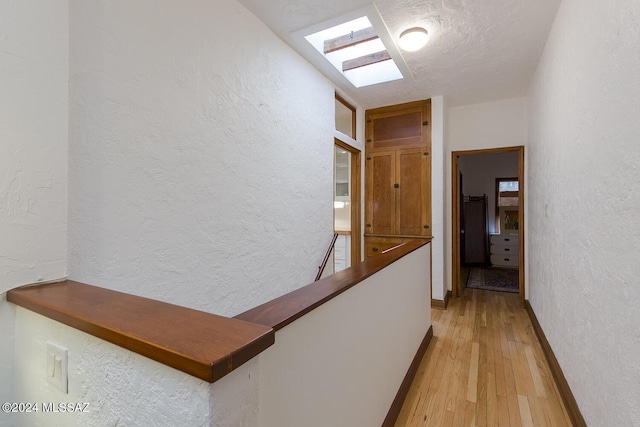 hallway featuring a textured ceiling, light hardwood / wood-style flooring, and a skylight