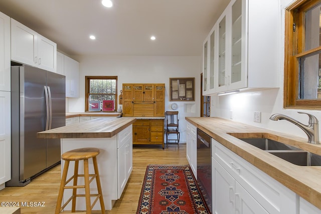 kitchen with white cabinetry, sink, stainless steel appliances, butcher block countertops, and a breakfast bar