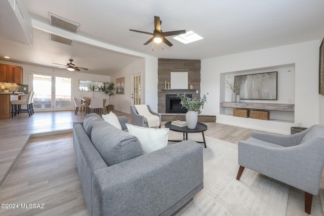 living room with a large fireplace, light hardwood / wood-style flooring, ceiling fan, and vaulted ceiling with skylight