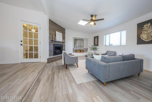 living room with a skylight, ceiling fan, a fireplace, and light hardwood / wood-style floors