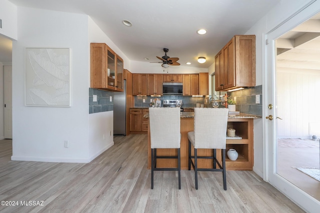 kitchen with backsplash, a breakfast bar area, light stone countertops, light hardwood / wood-style floors, and stainless steel appliances