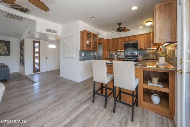 kitchen with a breakfast bar, sink, ceiling fan, appliances with stainless steel finishes, and light stone counters