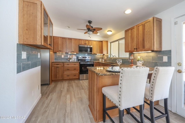 kitchen featuring a breakfast bar, stainless steel appliances, ceiling fan, light hardwood / wood-style flooring, and dark stone countertops