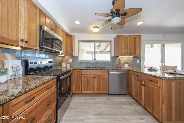 kitchen with light wood-type flooring, sink, appliances with stainless steel finishes, and dark stone counters