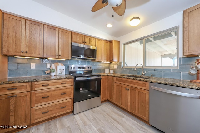 kitchen with light wood-type flooring, stainless steel appliances, vaulted ceiling, sink, and dark stone countertops