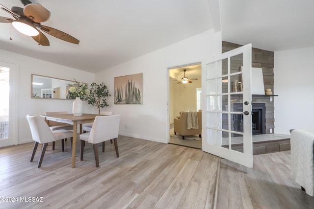 dining space featuring a fireplace, light hardwood / wood-style floors, ceiling fan, and lofted ceiling