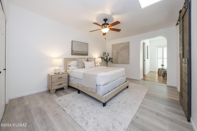 bedroom with ceiling fan, a barn door, and light hardwood / wood-style floors