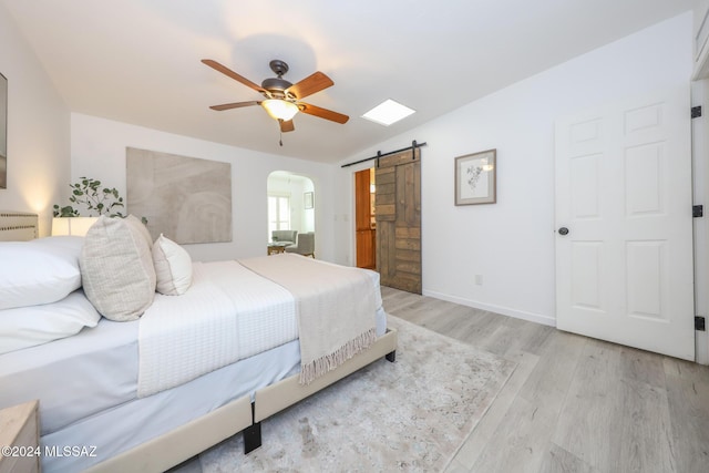 bedroom featuring ceiling fan, a barn door, light hardwood / wood-style floors, and lofted ceiling