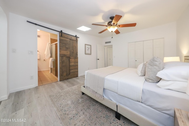 bedroom with ensuite bath, ceiling fan, a barn door, light hardwood / wood-style floors, and a closet