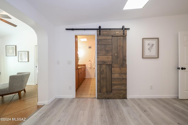 bedroom with a barn door, light hardwood / wood-style flooring, ensuite bath, and vaulted ceiling with skylight