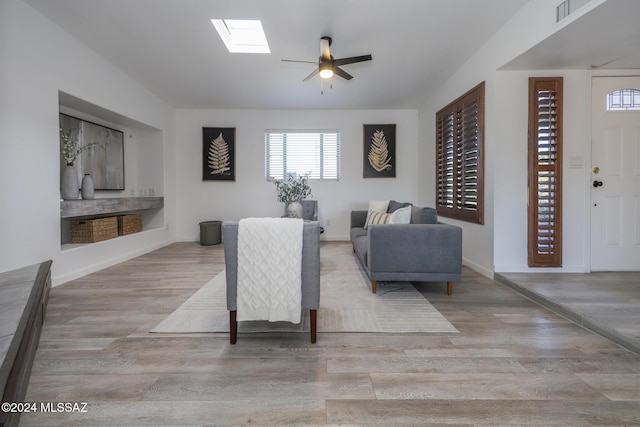 living room featuring a skylight, ceiling fan, and light hardwood / wood-style flooring