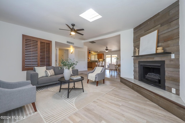 living room featuring ceiling fan, a large fireplace, wooden walls, and a skylight